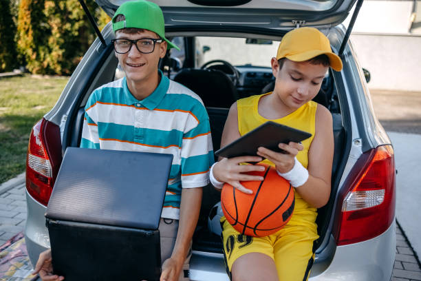 istock Teenagers sitting in car trunk using digital tablet before leaving on sport training 2173801251