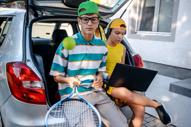 istock Teenagers sitting in car trunk using laptop before leaving on sport training 2173801266
