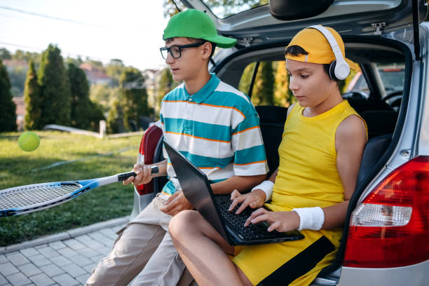 istock Teenagers sitting in car trunk using laptop before leaving on sport training 2173801269