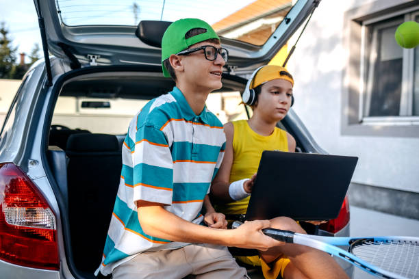 istock Teenagers sitting in car trunk using laptop before leaving on sport training 2173801273