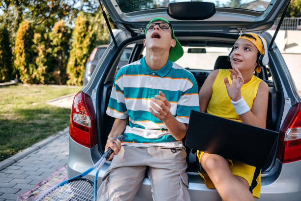 istock Teenagers sitting in car trunk using laptop before leaving on sport training 2173801282