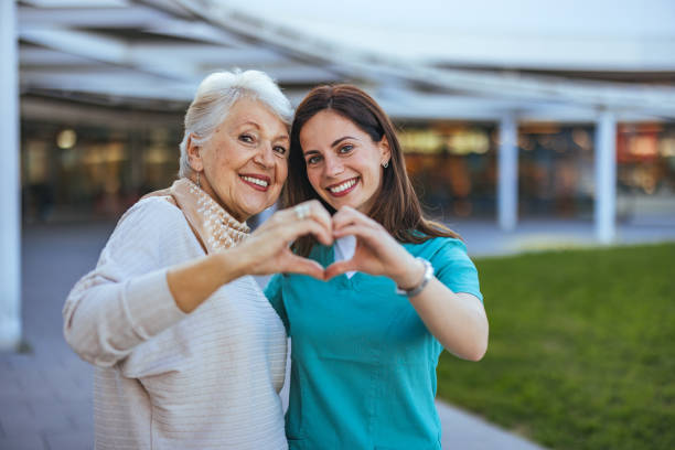 Joyful Senior Woman and Caregiver Making Heart Shape Outdoors Elderly woman and her caregiver happily form a heart shape with their hands, symbolizing care and companionship in an outdoor setting. loving life stock pictures, royalty-free photos & images