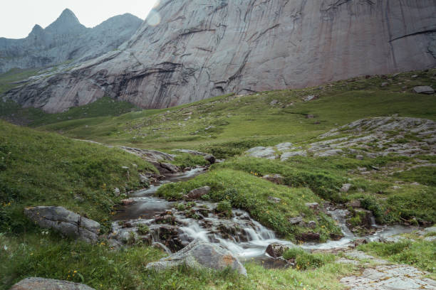 In the heart of Lofoten Islands, a serene stream winds through vibrant meadows, accompanied by majestic cliffs that rise dramatically above the landscape, inviting hikers to explore.