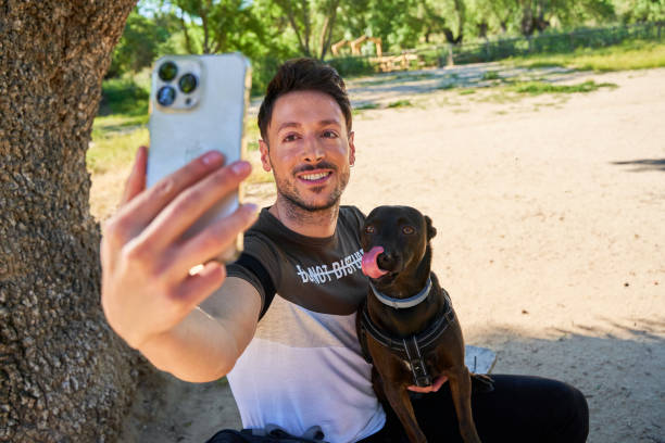 istock A male hiker with a backpack and a dog makes a selfie on the phone while sitting on a stone in the forest. Camping, travel, hiking. 2173872821