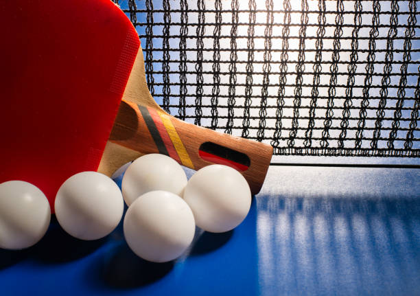 Two table tennis rackets and balls on a blue table with net.