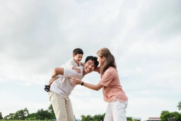 A happy Asian family enjoying a heartwarming moment, Little son on his father back, while the mother joins in the fun, laughing together. Joyful warmth and love of family time. A happy Asian family enjoying a heartwarming moment, Little son on his father back, while the mother joins in the fun, laughing together. Joyful warmth and love of family time.
