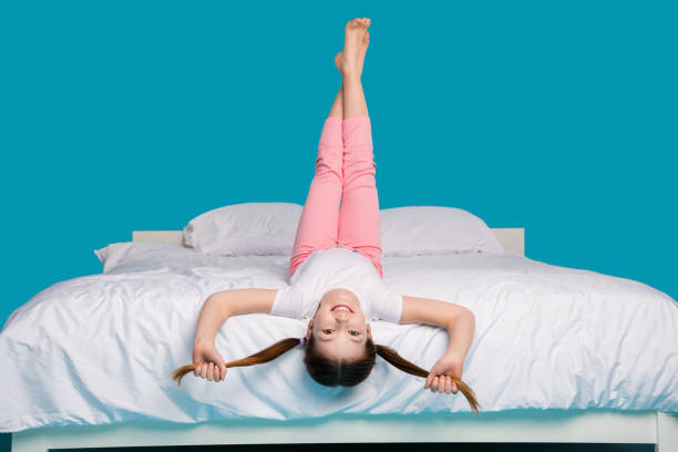 istock Full body photo of cute little girl pull tails upside down lying bed sleeping time dressed pajama isolated on blue color background 2173886708