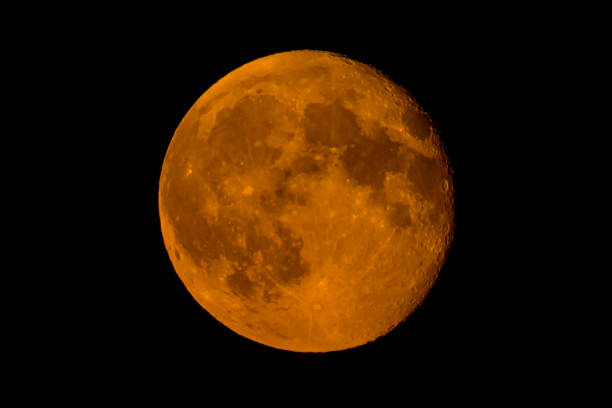 Moon with a clearly visible moon surface in the dark night sky. The moon is orange caused by moisture in the air just after sunset.