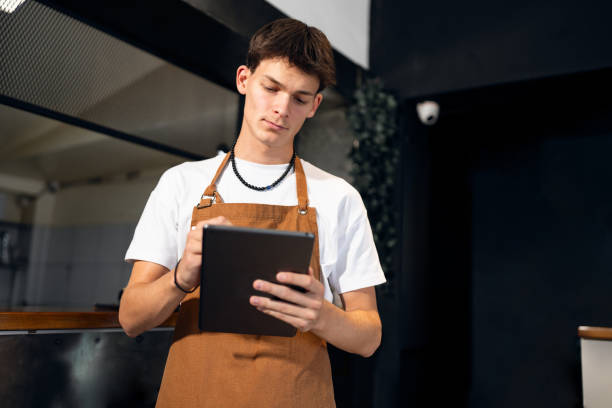 istock Caucasian teenage boy, using digital tablet while working at the fast food restaurant 2173891224