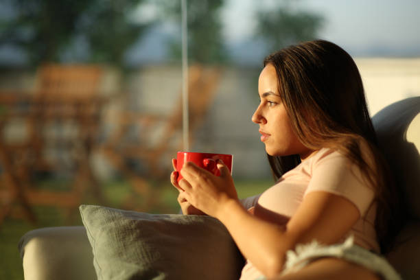 istock Serious woman drinking coffee looking through a window at sunset 2173893969