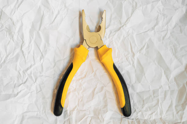 Yellow pliers on crumpled paper texture, top view