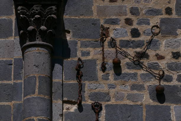 Basilica of Our Lady of Orcival, Orcival (Puy de Dome) Basilica of Our Lady of Orcival, Orcival (Puy de Dome) : chains and balls hanging on the facade of the church testify to miraculous releases of innocent prisoners or convicts orcival stock pictures, royalty-free photos & images