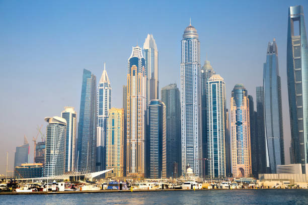 A distant view of the Dubai skyline photographed through warm desert haze. Modern skyscrapers and distinctive architecture rise above the city, including the curved roof of Ski Dubai in the foreground. A cinematic and atmospheric urban travel image from the United Arab Emirates.