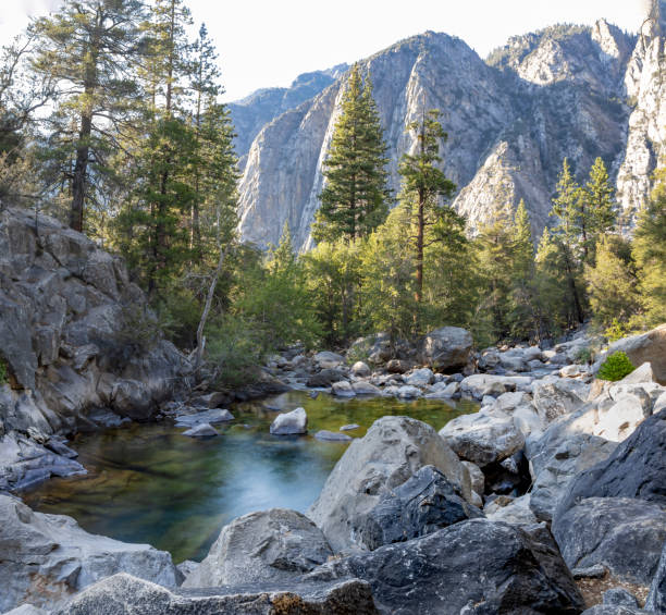 A stunning view of a calm pool of water surrounded by rugged rock formations at the bottom of Roaring Falls in King's Canyon National Park, California.