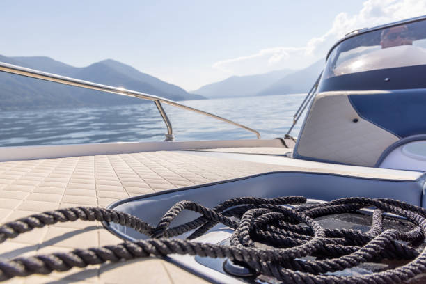 A coiled black rope rests on the deck of a boat, with a serene lake and misty mountains in the background. A peaceful moment of boating in nature.