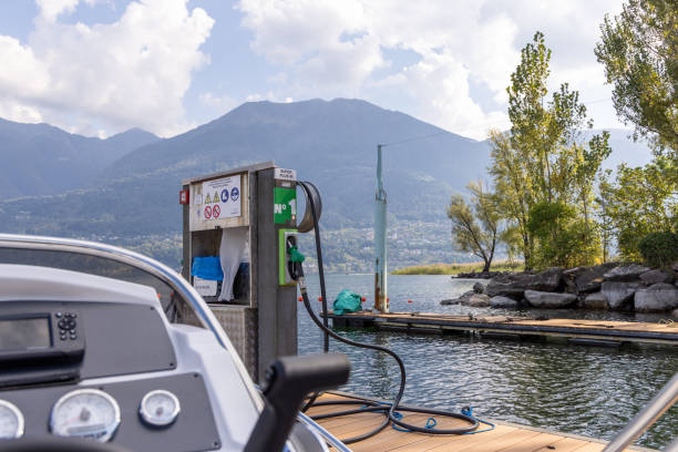 A boat is docked at a lake's fuel station, ready for refueling. Scenic mountains and calm waters create a picturesque backdrop.