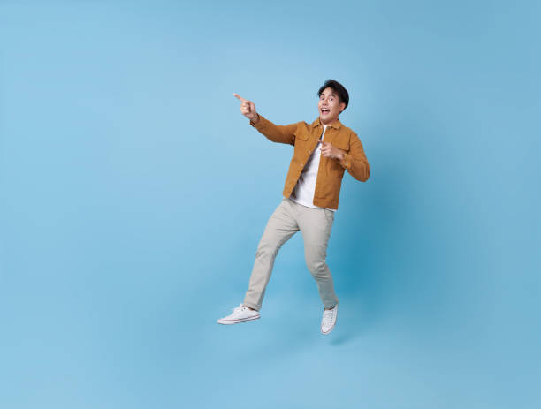 istock Full length Asian man jumping with hand pointing finger isolated on blue copy space background. 2173937524