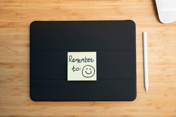 Yellow sticky note with a hand-drawn smiley face and the words remember to: is displayed on a tablet, serving as a reminder to stay positive