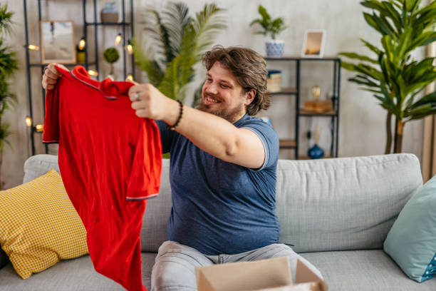istock Young Man Unboxing A Package With A New Shirt He Ordered Online 2173941382