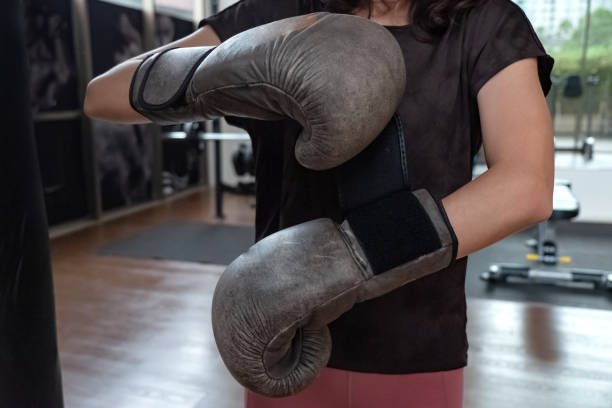 Shot of Unrecognizable woman putting on boxing glove by herself. Concept :  preparing for workout, self-preparation, boxing training, fitness routine, putting on gloves, combat sports, woman in sports, workout gear