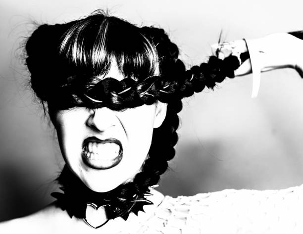 Portrait of a young woman from Generation Z. She has covered her eyes with her braided hair. She has opened her mouth and is gritting her teeth. This gives her face an aggressive expression. Blind and angry into an uncertain future.