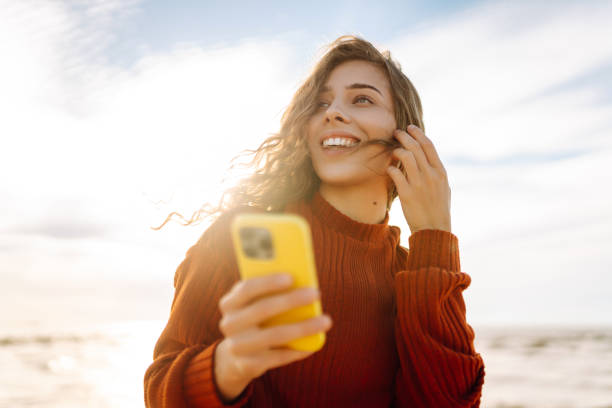 istock Young woman smiling and using her smartphone at the beach during sunset. 2173951718