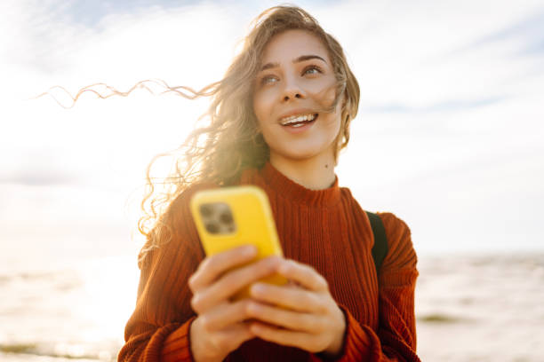 istock Young woman smiling and using her smartphone at the beach during sunset. 2173951748