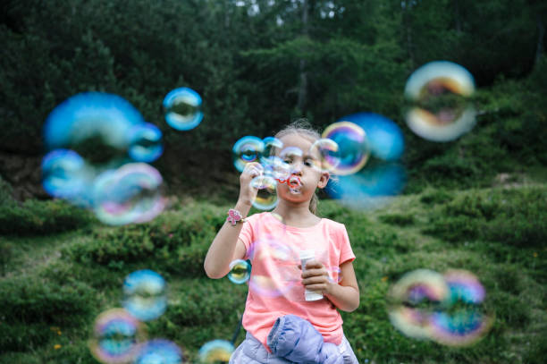 Toddler girl blowing soap bubbles in beautiful green summer nature.