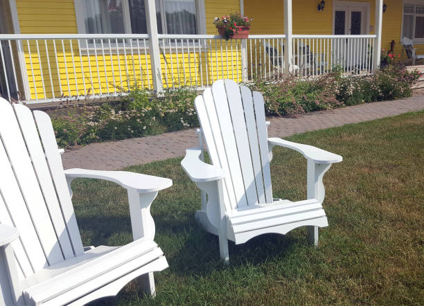 Rosebud, Alberta, Canada- August 12,2024:  Partial view of yellow country home with two new white Adirondack chairs on lawn in front yard.