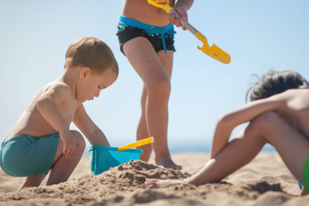 istock Toddler with his siblings playing with the sand on the beach. 2173964683