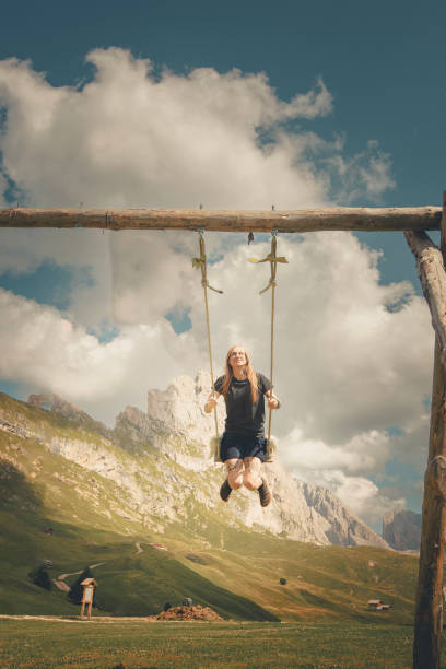 Young woman swings over mountain meadow, Dolomites