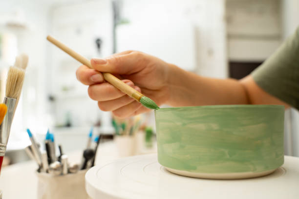 istock Using a brush to paint a ceramics bowl. Learning how to paint a handmade pottery project. Girl is decorating a clay product with bright green color. 2173975848