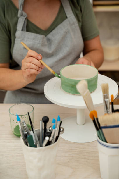 istock Using a brush to paint a ceramics bowl. Learning how to paint a handmade pottery project. Girl is decorating a clay product with bright green color. 2173975907