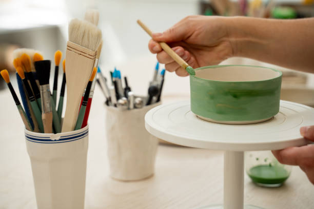 istock Using a brush to paint a ceramics bowl. Learning how to paint a handmade pottery project. Girl is decorating a clay product with bright green color. 2173975925