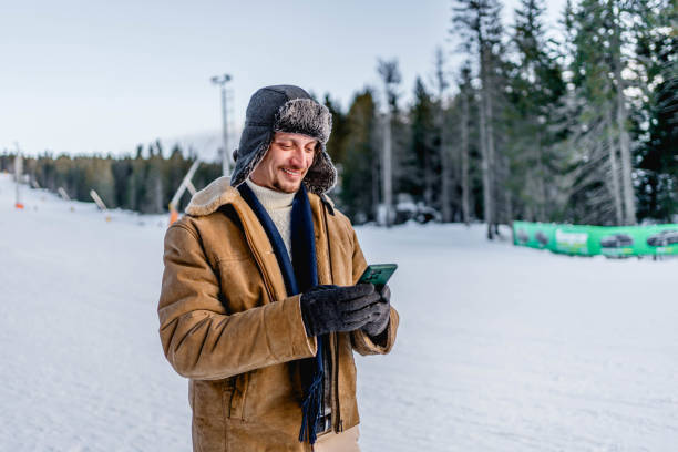 istock Young man using phone at a ski resort on the mountain 2173976917