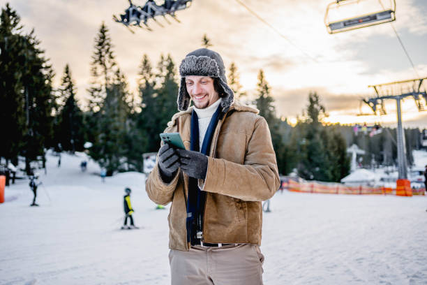 istock Young man using phone at a ski resort on the mountain 2173976943