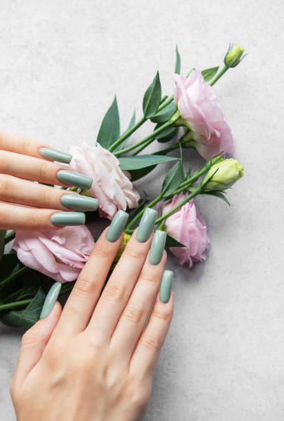 istock Elegant green manicured nails adorned with pastel flowers resting on a soft gray surface 2173978272