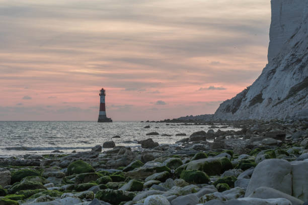 Beachy head lighthouse is illuminated by the warm glow of a setting sun, with the iconic chalk cliffs of the sussex coastline in the background