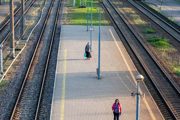 Riga, Latvia - September 30, 2020: Two people wait on the platform near train tracks in bright daylight.