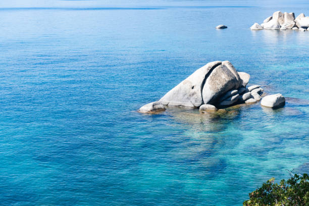 This is a photograph of Lake Tahoe with boulders sticking out of the clear blue water on a sunny summer day in Nevada.
