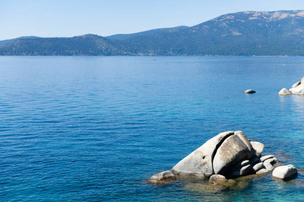 This is a photograph of Lake Tahoe with boulders sticking out of the clear blue water on a sunny summer day in Nevada.
