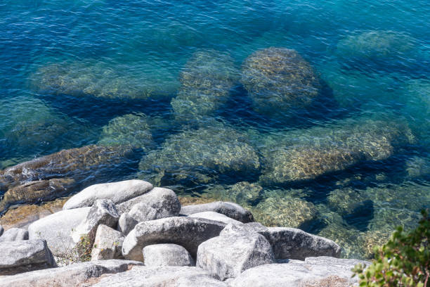 This is a photograph of Lake Tahoe with boulders sticking out of the clear blue water on a sunny summer day in Nevada.
