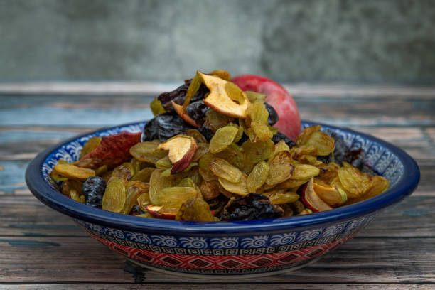 Ceramic blue bowl with dry fruit plum grape apple on old wooden table near stone wall