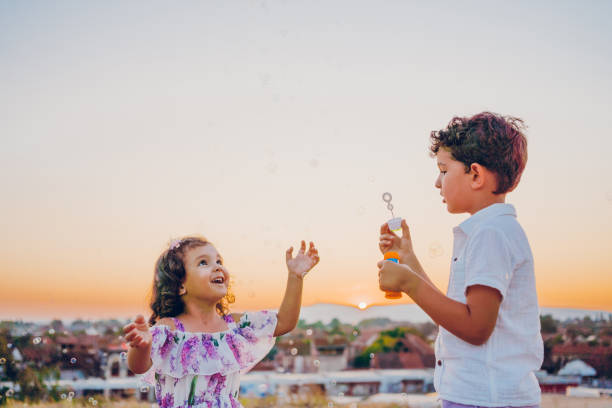 Little boy make bubbles for little girl at sunset