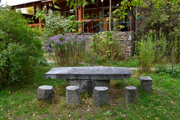 A stone table with matching stools sits amidst vibrant autumn greenery.