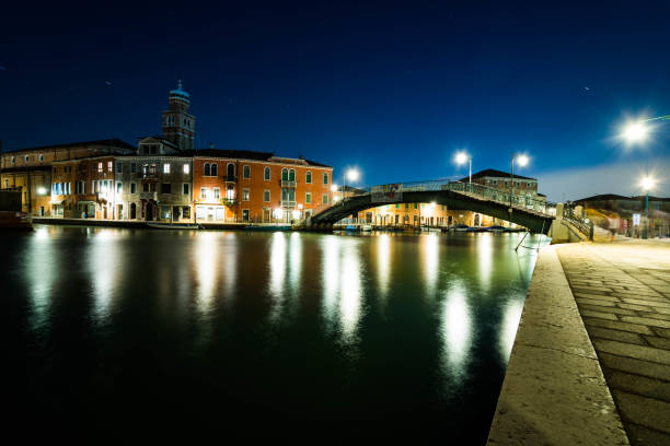 Long exposure of a canal reflecting the city lights at night in venice, italy