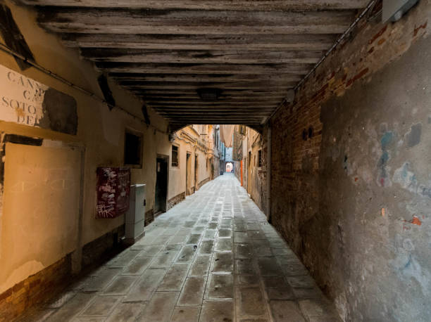 Long, narrow street in venice with old buildings is leading to a bridge and open area in the distance