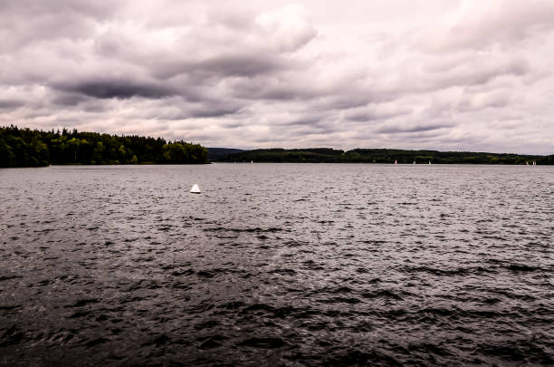 A lake with a boat in the water and a cloudy sky. The sky is overcast and the water is calm
