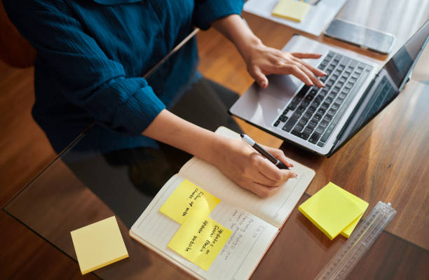 Focused Woman Working on Laptop with Yellow Sticky Notes stock photo