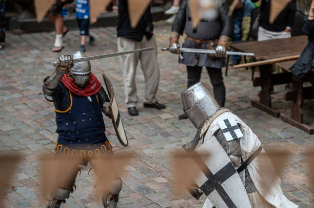A man in knight armor and a woman in elegant medieval attire express a humorous scene on a vibrant stage, showcasing retro-themed costumes.